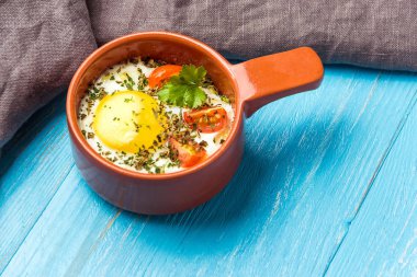 Mavi ahşap masa üzerinde seramik cocotte porsiyonluk pişmiş yumurta, kahvaltı. metin için boşluk kopyalama.