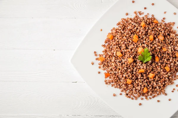 Beyaz ahşap masada beyaz bir tabak lezzetli karabuğday lapası. Üst görünüm.