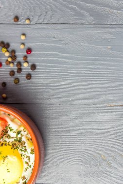 Gri ahşap masa üzerinde seramik cocotte porsiyonluk pişmiş yumurta, kahvaltı. Üst görünüm, metin için alan kopyalama.
