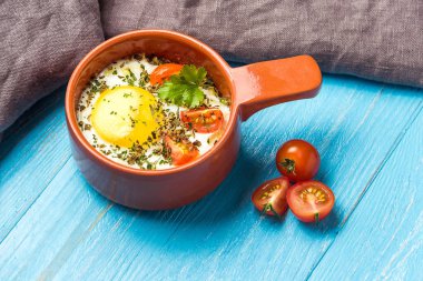 Mavi ahşap masa üzerinde seramik cocotte porsiyonluk pişmiş yumurta, kahvaltı.