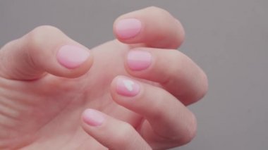 Yakın çekimde bir kadın eli, pembe pastel jel ojeli, eski ve uzun ömürlü tırnaklarıyla görülüyor..