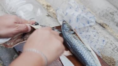 Şef çiğ başsız uskumruyu kesme tahtasında bıçakla keser.