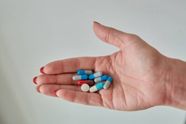 Kadın elinin üzerindeki renkli ilaç hapları, tabletler ve kapsüller beyaz arka planda. Yakın plan..