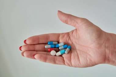 Kadın elinin üzerindeki renkli ilaç hapları, tabletler ve kapsüller beyaz arka planda. Yakın plan..