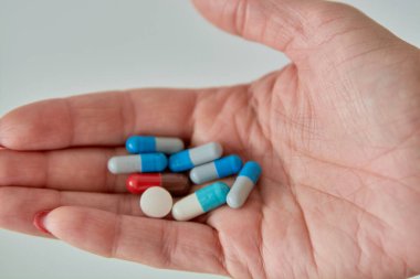 Kadın elinin üzerindeki renkli ilaç hapları, tabletler ve kapsüller beyaz arka planda. Yakın plan..