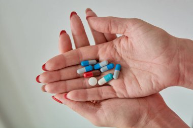 Kadın elinin üzerindeki renkli ilaç hapları, tabletler ve kapsüller beyaz arka planda. Yakın plan..