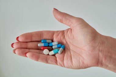 Kadın elinin üzerindeki renkli ilaç hapları, tabletler ve kapsüller beyaz arka planda. Yakın plan..