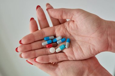Kadın elinin üzerindeki renkli ilaç hapları, tabletler ve kapsüller beyaz arka planda. Yakın plan..
