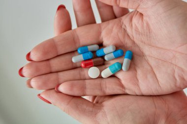 Kadın elinin üzerindeki renkli ilaç hapları, tabletler ve kapsüller beyaz arka planda. Yakın plan..