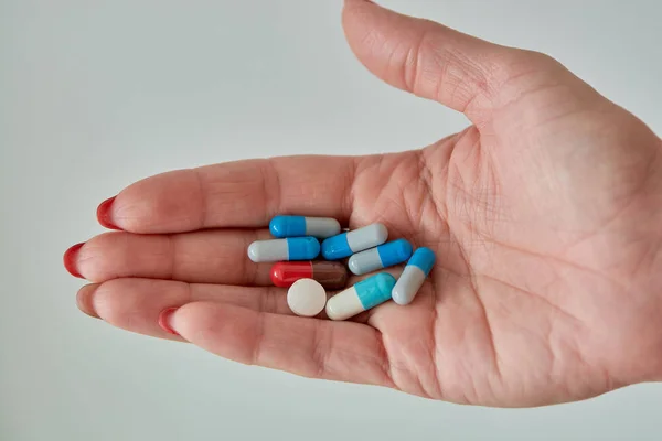 Kadın elinin üzerindeki renkli ilaç hapları, tabletler ve kapsüller beyaz arka planda. Yakın plan..