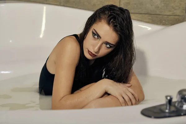 Молода жінка в чорному купальнику позує у ванні з молоком . — стокове фото