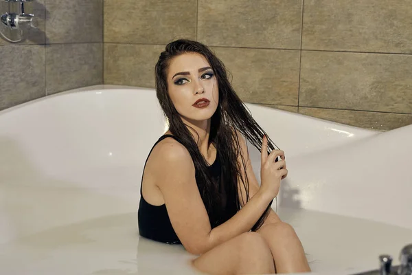 Young woman in a black bathing suit posing in the bath of milk. — Stock Photo, Image