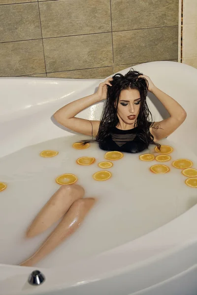 Mulher jovem no banho de leite e com fatias de laranjas . — Fotografia de Stock