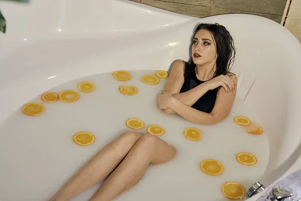 Mulher jovem no banho de leite e com fatias de laranjas . — Fotografia de Stock