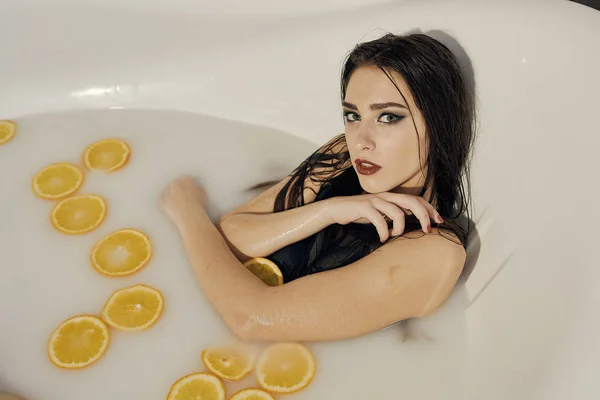 Mujer joven en el baño de leche y con rodajas de naranjas . — Foto de Stock