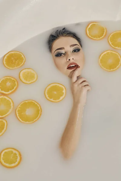 Mulher jovem no banho de leite e com fatias de laranjas . — Fotografia de Stock