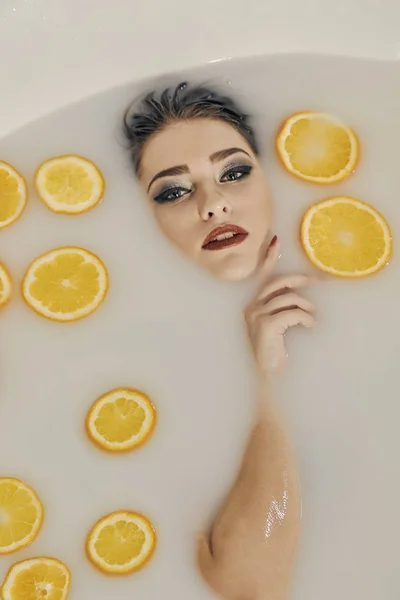 Mujer joven en el baño de leche y con rodajas de naranjas . —  Fotos de Stock