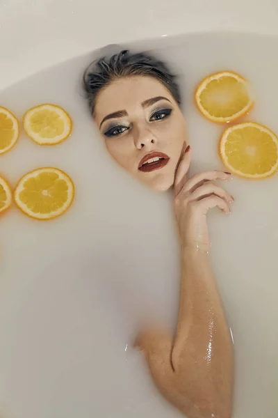 Ung kvinna i badet mjölk och med apelsiner skivor. — Stockfoto