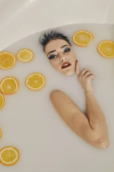 Jonge vrouw in het bad van melk en sinaasappels segmenten. — Stockfoto