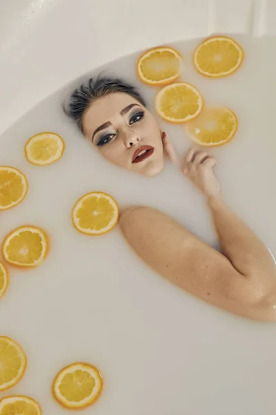 Mujer joven en el baño de leche y con rodajas de naranjas . —  Fotos de Stock