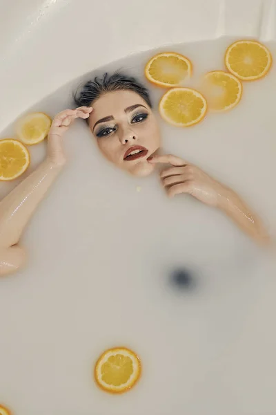 Молодая женщина в ванне из молока и с апельсинами ломтики . — стоковое фото