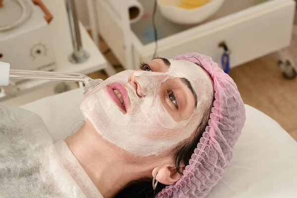 Mujer joven en el salón de belleza hace rejuvenecedor, procedimiento de tonificación darsonval en la cara . — Foto de Stock