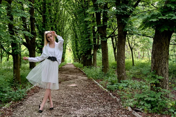 Blonde woman walks alone along the chestnut alley in the city park. Young woman modern portrait.