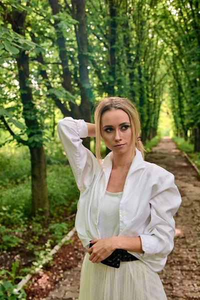 Blonde woman walks alone along the chestnut alley in the city park. Young woman modern portrait. — Stock Photo, Image