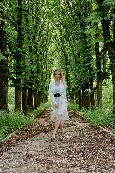 Blonde woman walks alone along the chestnut alley in the city park. Young woman modern portrait.