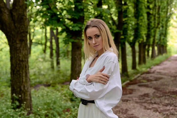 Blonde woman walks alone along the chestnut alley in the city park. Young woman modern portrait.