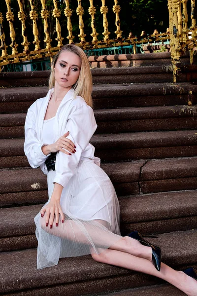 Sarışın kadın eski granit merdivenmerdivenlerinde oturur. Genç kadın modern portre.