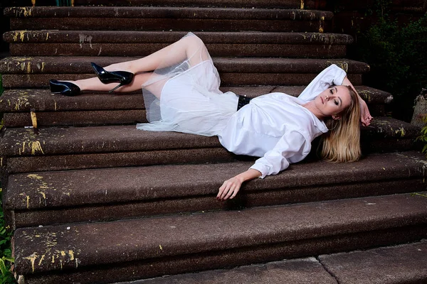 Blonde woman sits on the steps of the old granite stair. Young woman modern portrait. — Stock Photo, Image