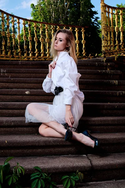 Sarışın kadın eski granit merdivenmerdivenlerinde oturur. Genç kadın modern portre.