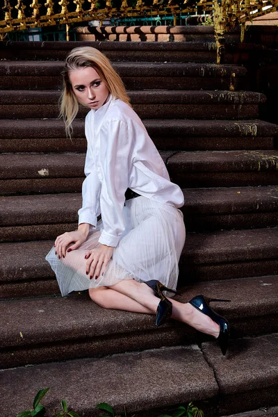 Sarışın kadın eski granit merdivenmerdivenlerinde oturur. Genç kadın modern portre.