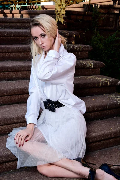 Blonde vrouw zit op de trappen van de oude granieten trap. Jonge vrouw modern portret. — Stockfoto