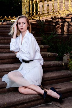 Sarışın kadın eski granit merdivenmerdivenlerinde oturur. Genç kadın modern portre.