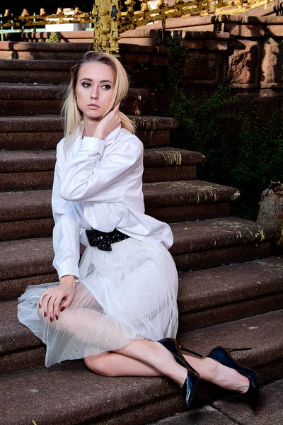 Blonde vrouw zit op de trappen van de oude granieten trap. Jonge vrouw modern portret. — Stockfoto