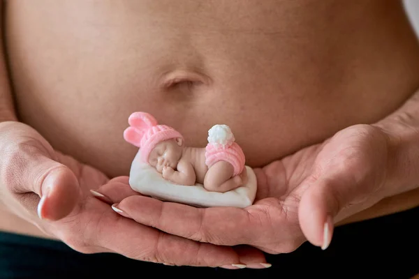 Schwangere junge Wollschwester hält eine Figur aus Seife in Form eines neugeborenen Mädchens. — Stockfoto