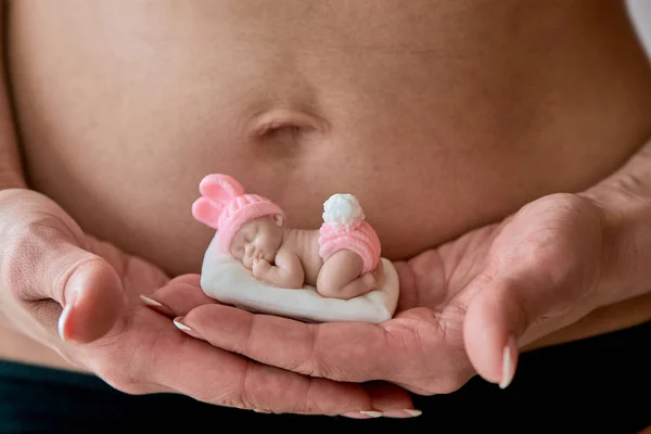 Pregnant young woomen holds a figurine of soap in the shape of a newborn baby girl. — Stock Photo, Image