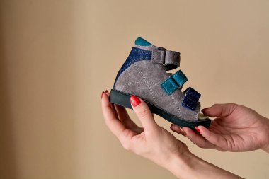 Kadın elinde hakiki deriden yapılmış ortopedik çocuk ayakkabısı sandaletleri tutuyor. Telif alanı olan hafif arka planda izole edilmiş rahat ayakkabılar. Görüntü reklam için uygun.