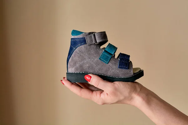 Kadın elinde hakiki deriden yapılmış ortopedik çocuk ayakkabısı sandaletleri tutuyor. Telif alanı olan hafif arka planda izole edilmiş rahat ayakkabılar. Görüntü reklam için uygun.