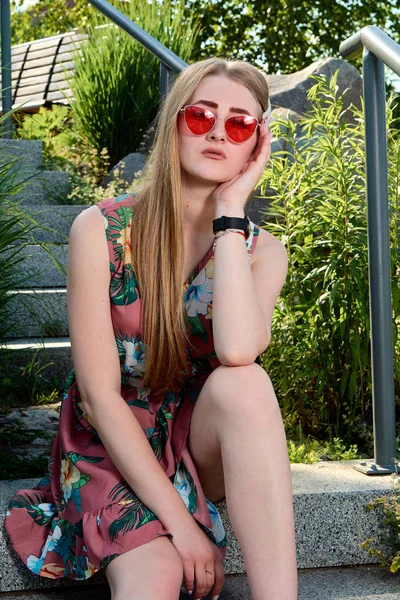 Fiatal vonzó nő. Piros napszemüveg, színes ruhában. Lány portréja. — Stock Fotó