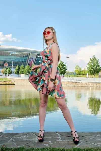 Fiatal vonzó nő. Piros napszemüveg, színes ruhában. Lány portréja. Futballstadion háttér. — Stock Fotó