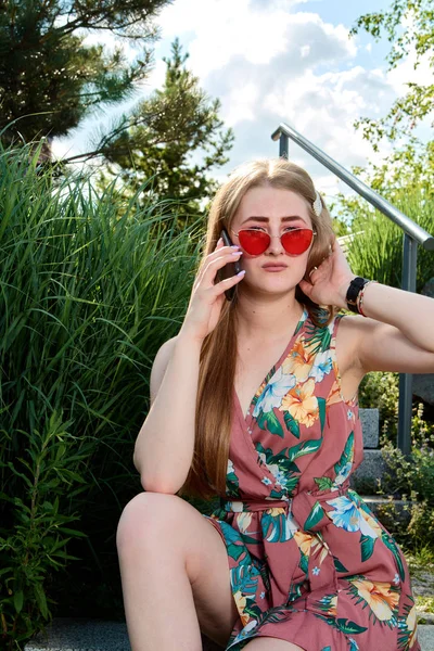 Jovem mulher atraente. Óculos de sol vermelhos, vestido de cor, telefone celular, 5G, 4G, 3G, 2G, rede LTE . — Fotografia de Stock