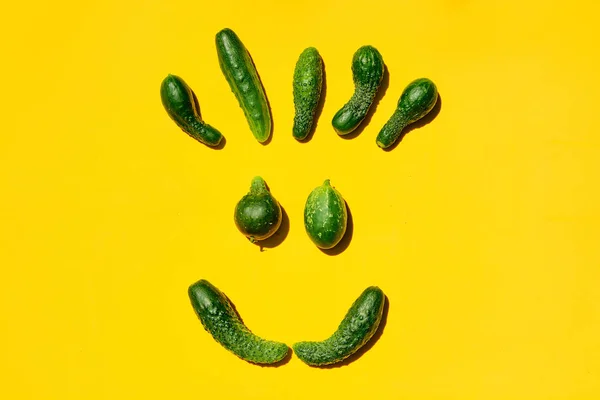 Different sizes and forms cucumbers on a yellow background forms a smiling face.