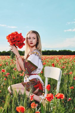 Yeşil buğday ve yabani haşhaş bir alanda beyaz kısa elbiseli uzun saçlı sarışın genç kadın.