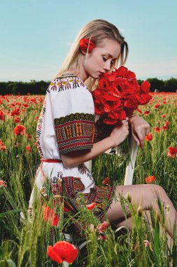 Yeşil buğday ve yabani haşhaş bir alanda beyaz kısa elbiseli uzun saçlı sarışın genç kadın.