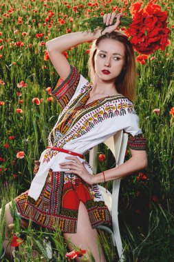 Yeşil buğday ve yabani haşhaş bir alanda beyaz kısa elbiseli uzun saçlı sarışın genç kadın.