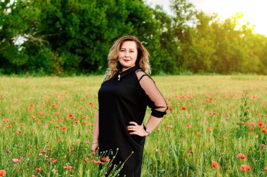 Artı yeşil buğday ve yabani haşhaş bir alanda siyah elbiseli bir kadın. Kilolu şişman kadın.