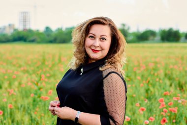 Artı yeşil buğday ve yabani haşhaş bir alanda siyah elbiseli bir kadın. Kilolu şişman kadın.